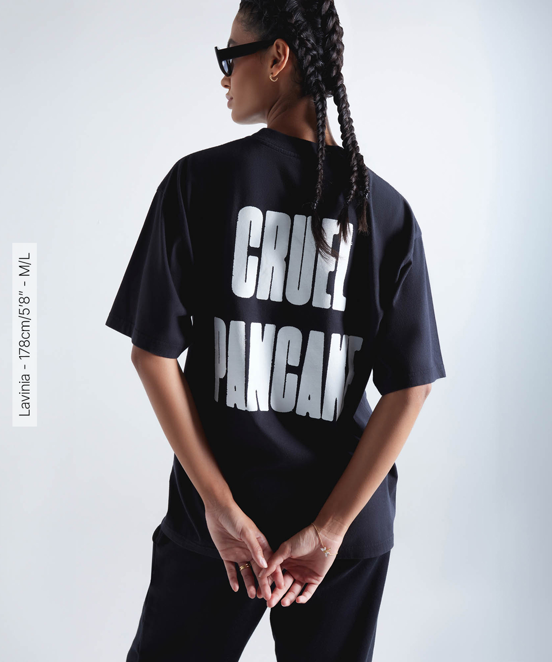 Femme portant un t-shirt noir oversize Cruel Pancake avec texte blanc au dos, mains jointes.